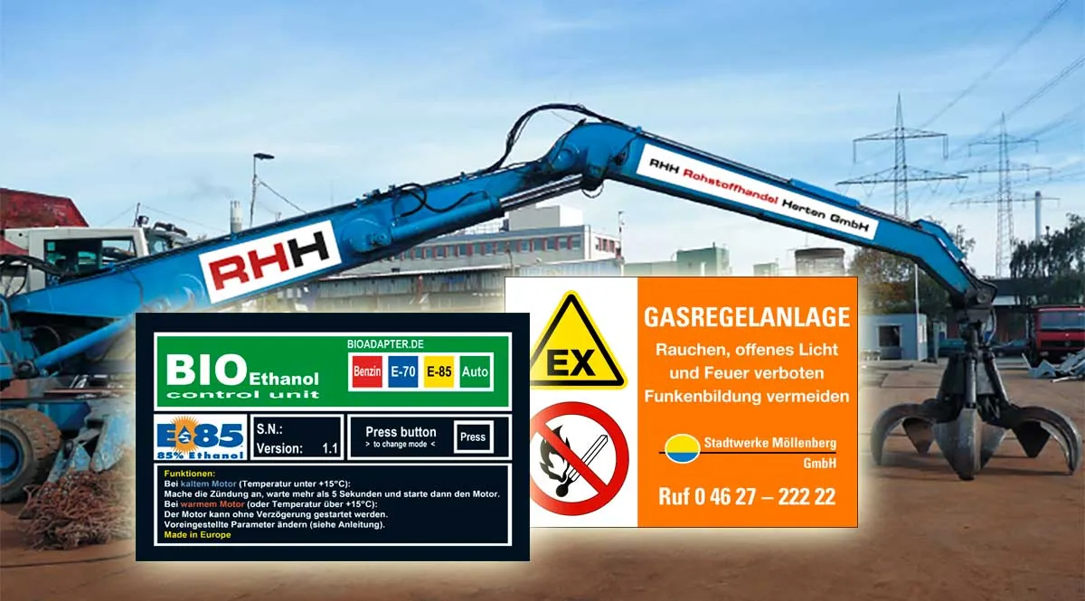 Bagger mit Firmenaufklebern am Ausleger, davor ein Bedienschild für ein Ethanol-Steuergerät und ein Warnschild Gasregelanlage