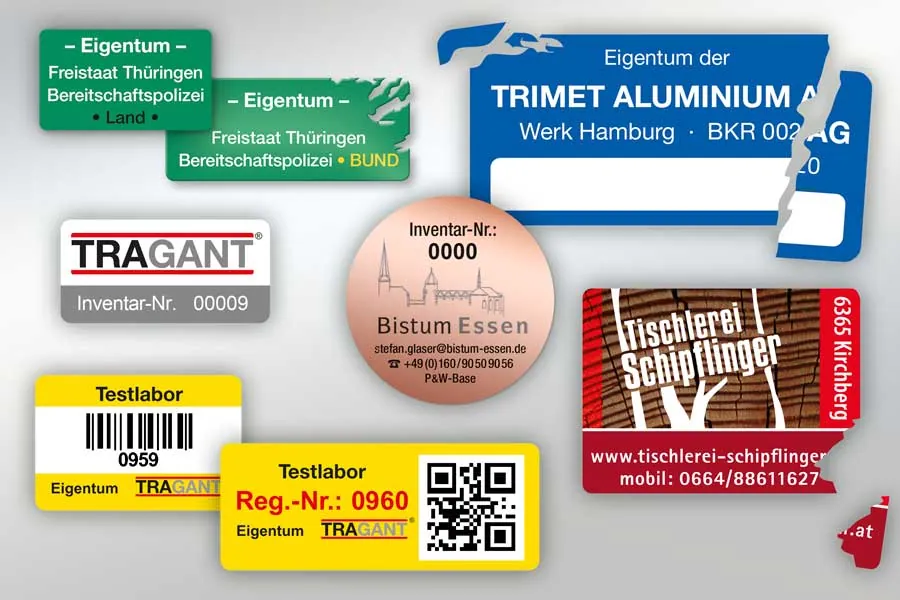 Eigentumsaufkleber mit Firmenname, Inventarnummer, Barcode und QR-Code, einige davon beim Ablöseversuch zerrissen