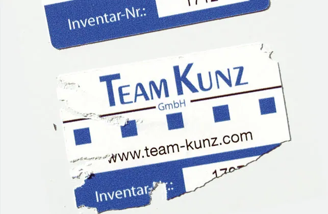Inventaraufkleber mit Firmenlogo, einer beim Ablöseversuch zerrissen